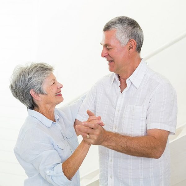 Cheerful senior couple dancing together at home in living room